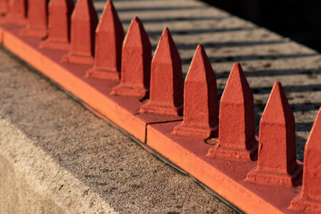 An image displaying a form of hostile architecture in which red metal spikes have been attached to a concrete ledge to prevent people sitting and sleeping